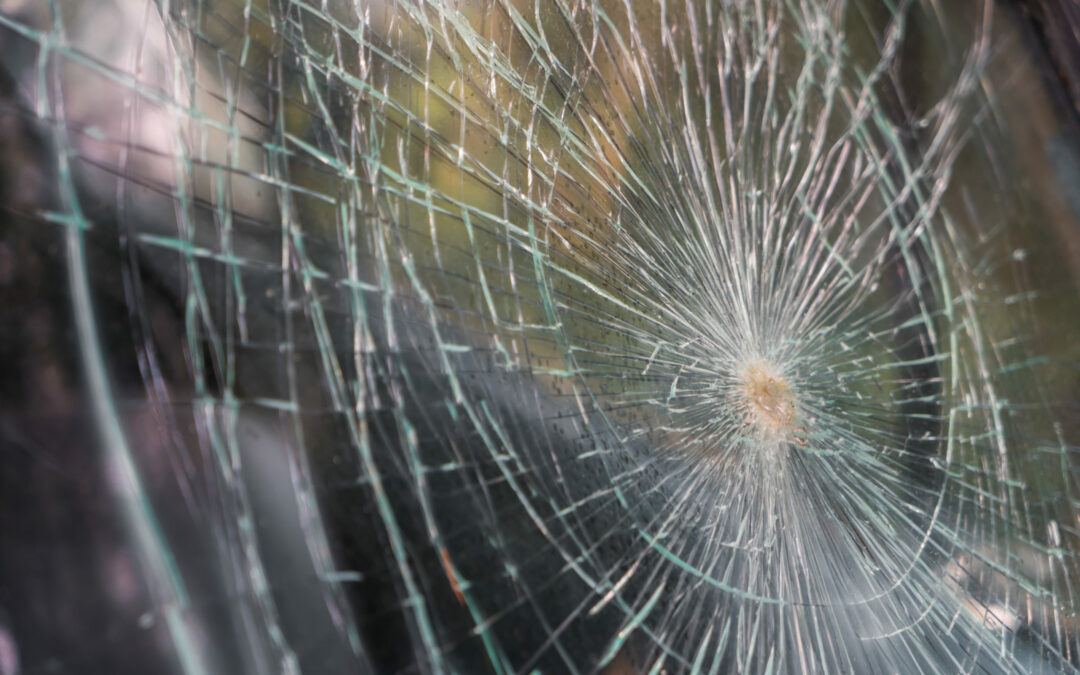 Close-up of a shattered glass surface with numerous cracks radiating from a central impact point. The web-like pattern of the cracks creates a complex, intricate design, suggesting this could be part of a breaking news scene in Palm Coast or Flagler County. The blurry background hints it may belong to a window or windshield.