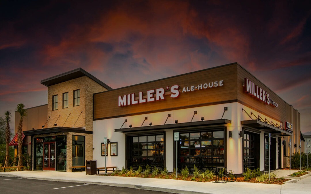 A restaurant named "Miller's Ale House" is pictured during sunset The building features large windows, modern architecture, and outdoor lighting The sky in the background has vibrant hues of red, orange, and purple, enhancing the peaceful ambiance