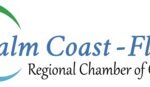 Logo of the Palm Coast Flagler Regional Chamber of Commerce The text is in blue, with three curved, swoosh like accents in green, orange, and light blue to the left of the text