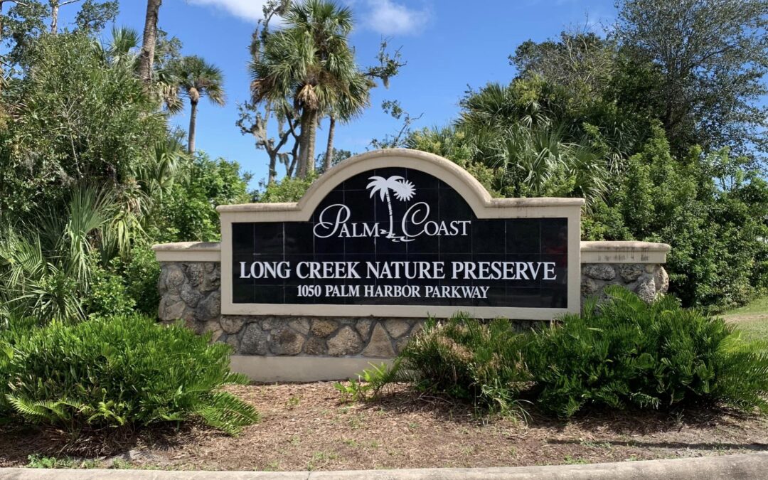 Sign for Palm Coast Long Creek Nature Preserve at Palm Harbor Parkway The stone sign is surrounded by lush greenery and tall trees under a partly cloudy sky