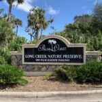 Sign for Palm Coast Long Creek Nature Preserve at Palm Harbor Parkway The stone sign is surrounded by lush greenery and tall trees under a partly cloudy sky