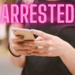 A person holding a smartphone with teal nail polish applied, wearing a dark shirt The word "ARRESTED" is prominently displayed in pink letters at the top of the image