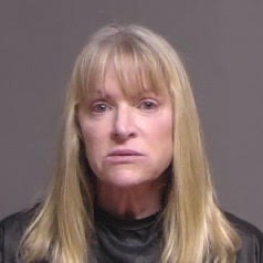 A woman with long, straight blonde hair and bangs is wearing a black top She is looking directly at the camera against a neutral background