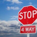 A red stop sign with the words " WAY" beneath it stands against a backdrop of a cloudy blue sky