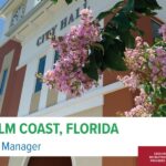 City Hall building in Palm Coast, Florida, featuring blooming pink flowers in the foreground The image announces a City Manager position with a banner displaying "Executive Recruitment Provided by SGR