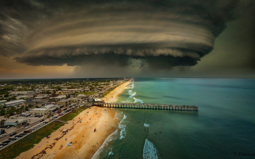 A massive, swirling storm cloud looms over a coastal city, casting shadows over a beach and pier The turbulent sky contrasts with the calm ocean and buildings, creating a dramatic scene