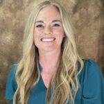 A person with long blonde hair is smiling at the camera, wearing a teal top The background is a textured brown color