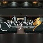 Interior view of The Fitzgerald Performing Arts Center, featuring rows of green seats facing a stage The venue name is prominently displayed in elegant white and gold lettering