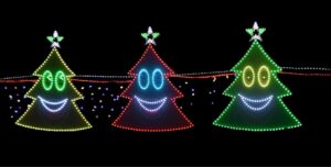 Three illuminated Christmas tree shapes with smiling faces, outlined in green, red, and green lights Each tree has a star on top, and they are connected by a string of lights against a black background