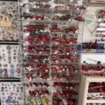 A display shelf filled with numerous red model fire trucks, organized neatly in rows The wall next to it features a collection of various pins and badges A small sign with colorful text is visible on the right