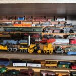 A wooden shelf filled with assorted model trains, featuring both vintage and modern designs The trains are displayed on different shelves, showcasing a variety of colors and styles, highlighting engines and carriages