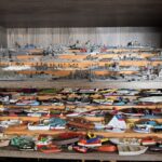 Shelves filled with an extensive collection of model ships and boats, including battleships, sailboats, and various vessels Each model is intricately detailed and displayed in organized rows on wooden shelves