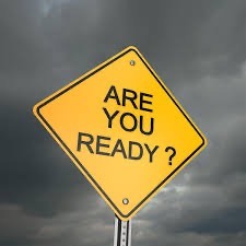 A yellow diamond shaped road sign against a cloudy sky, displaying the text "ARE YOU READY?" in bold black letters