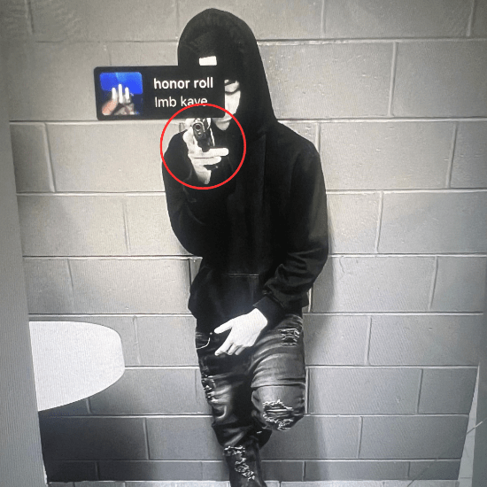 Person in a hooded sweatshirt and mask leans against a brick wall, holding a phone up for a selfie A red circle highlights the camera area Text on the image reads "honor roll Imb kave " The person wears ripped jeans