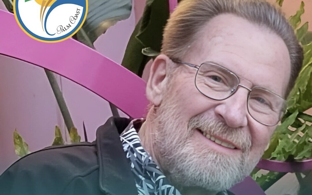 A man with glasses and a beard smiles, wearing a patterned shirt and a dark jacket The background has vibrant plants and a pink structure A logo with a palm tree and the text "Palm Coast" is in the upper left corner